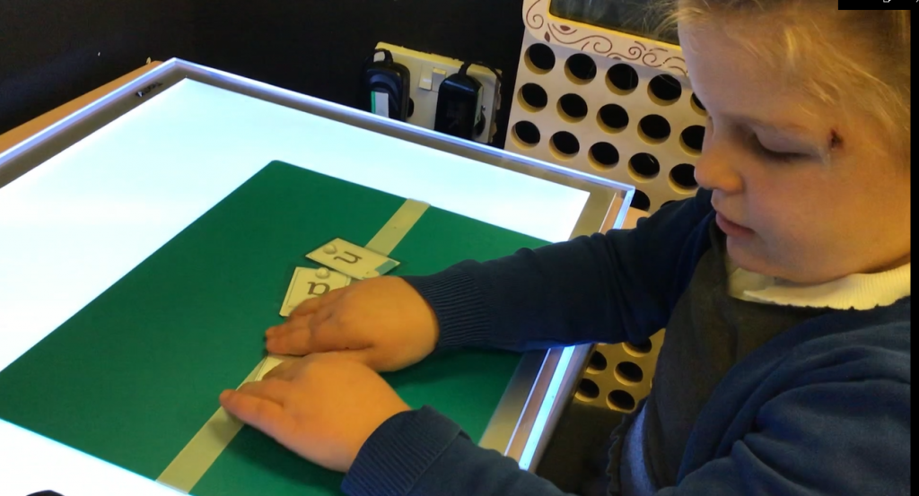 Photo of Sienna at school working with letter cards. Sienna is using a light panel.